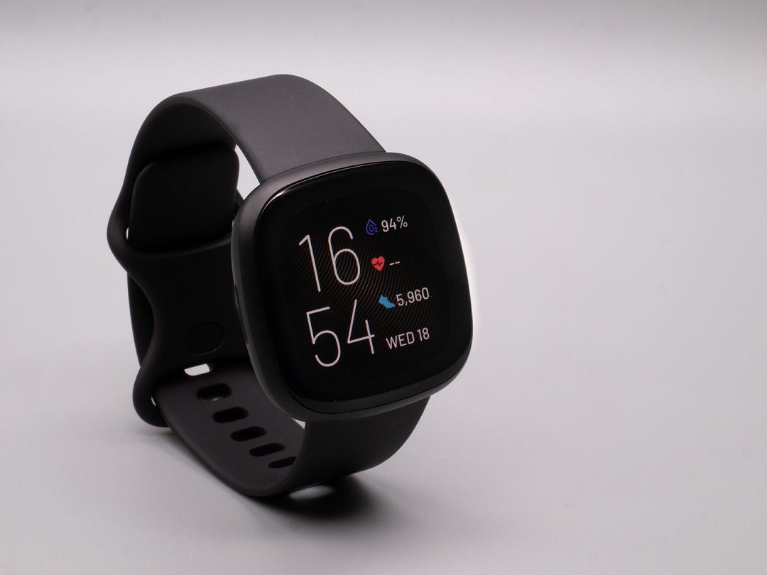 A black Fitbit Versa 3 standing on a gray background