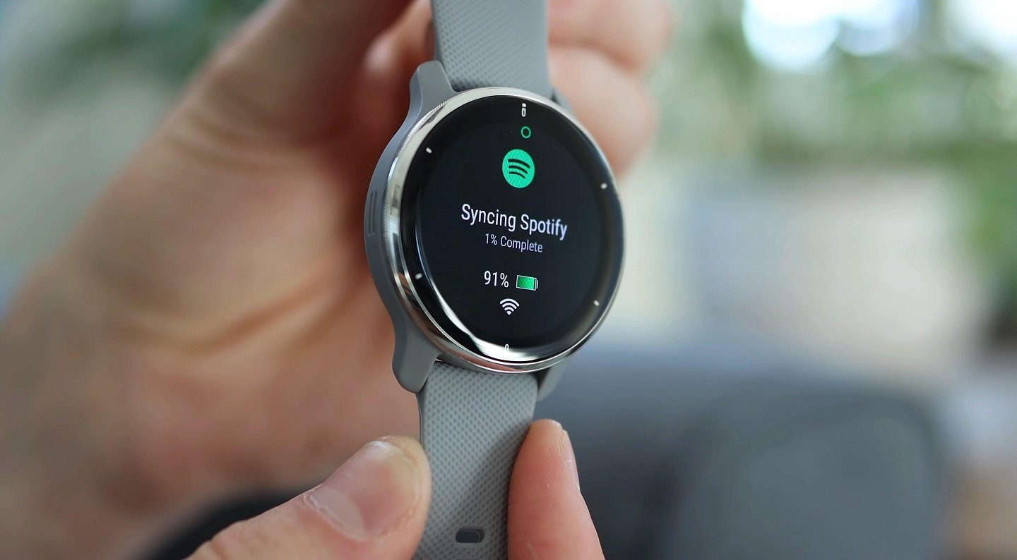 A person holding Garmin Venu 2 Plus with Spotify app running on the smartwatch