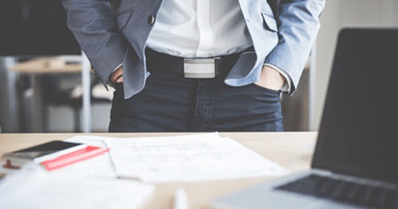 A man in a suit standing behind work desk with hands in pockets