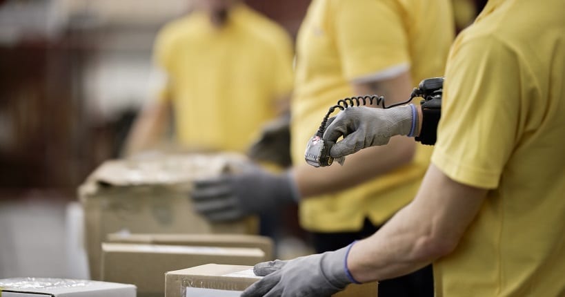 a worker with wearable scanner attached on his hand scanning a package